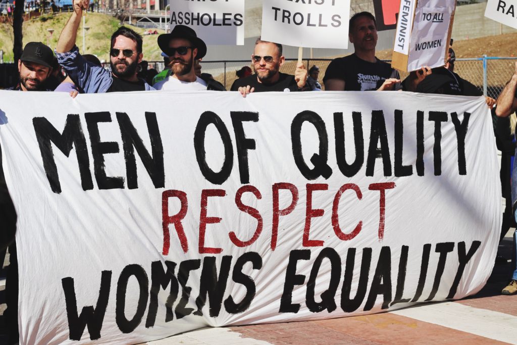 Men protesting why reproductive rights are important while holding a sign that says 'Men of quality respect womens equality' 