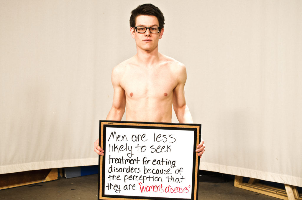 Teen boy hold sign reading 'men are less likely to see treatment for eating disorders' entity