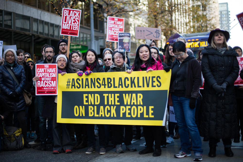 Protestors holding a sign that says "Asians for Black Lives. End the War on Black People"