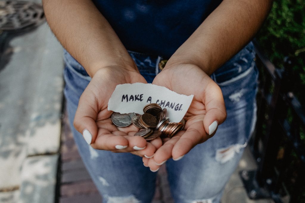 Hands holding coins with a piece of paper saying "make a change"