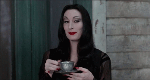 Classic Halloween Queen Morticia Addams smiling and drinking a cup of tea.