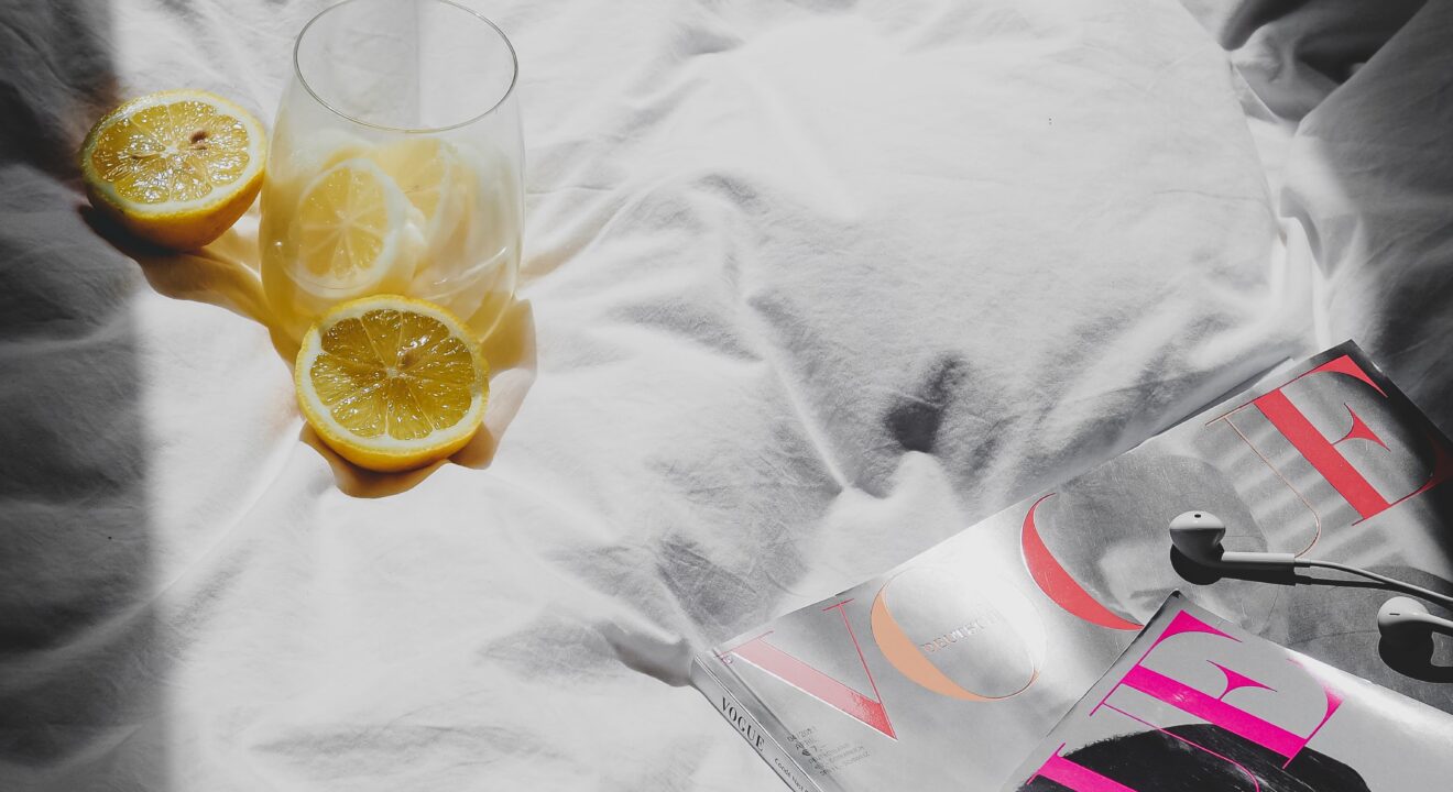 A magazine and glass of detox water on the bed ready to read and enjoy a day of self care sunday.