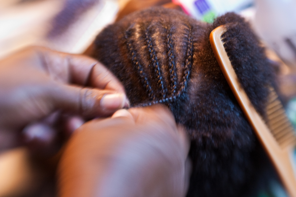 Black women's hair being braided into cornrows