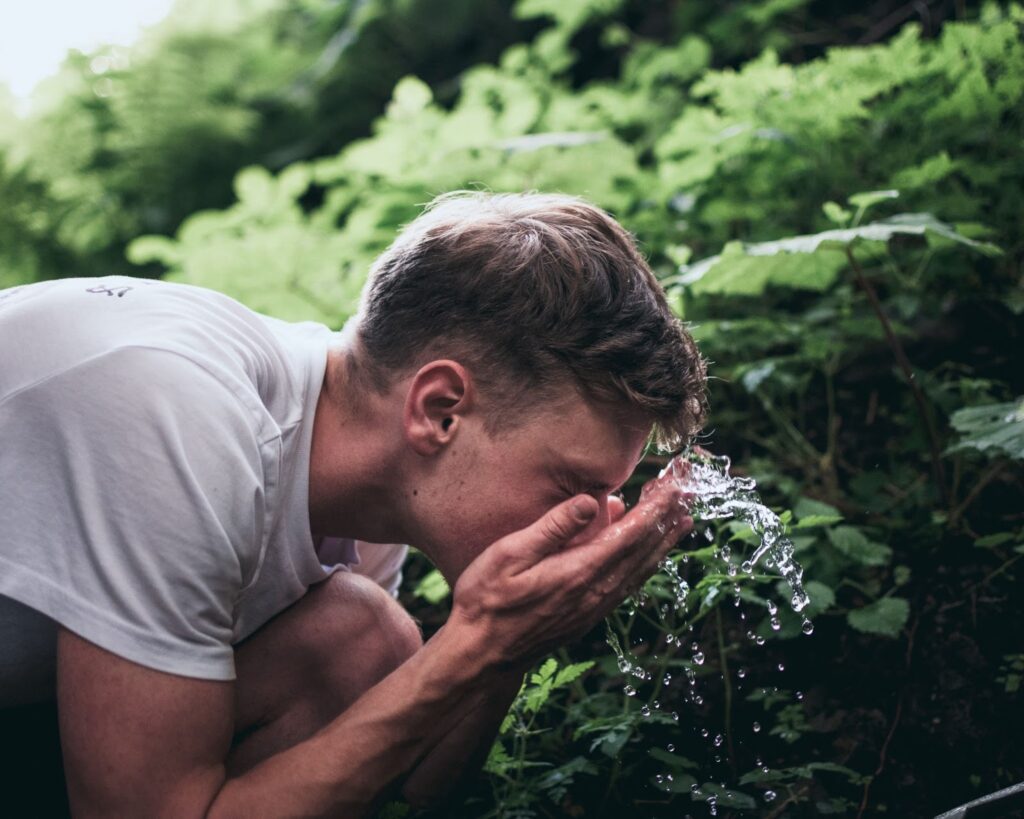 Image of man washing face outside to illustrate the first step in ENTITY Mag's skincare routine order.