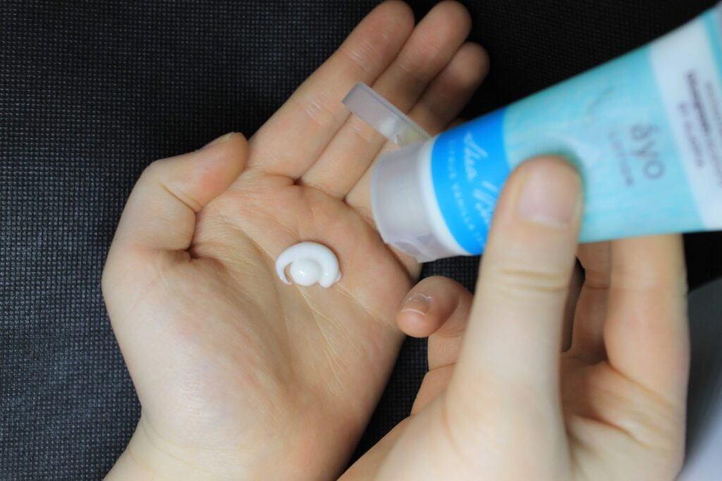 Top view of a woman's hands, one hand is squeezing moisturizer out of a blue bottle and the other has a dollop of white product on her palm. 